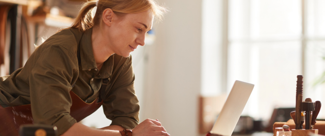 Woman looks at laptop on work bench.